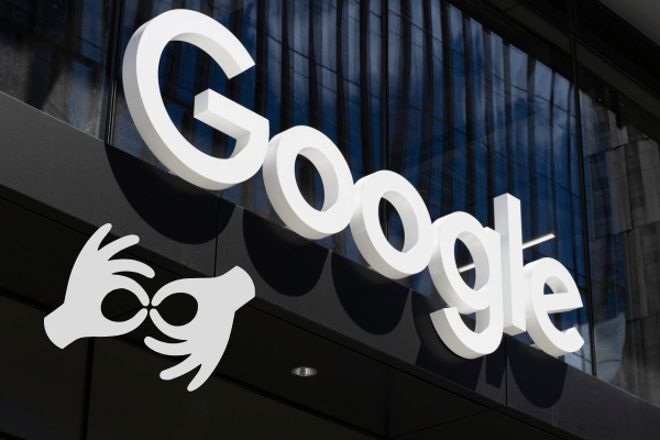 Large white 3D Google logo mounted on a glass building exterior, with a white sign language interpretation icon overlaid in the bottom-left corner.